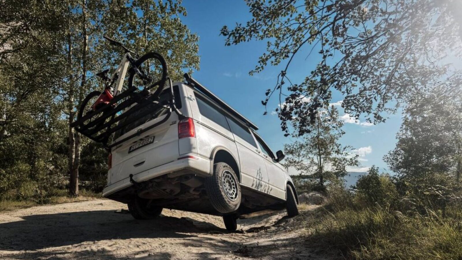 VW California T6.1 na zawieszeniu podnoszącym Twin-Monotube-Projekt z oponami All-Terrain na leśnej drodze