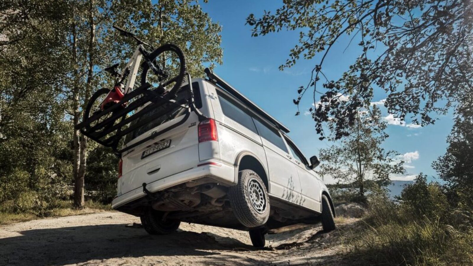 VW California T6.1 na zawieszeniu podnoszącym Twin-Monotube-Projekt z oponami All-Terrain na leśnej drodze